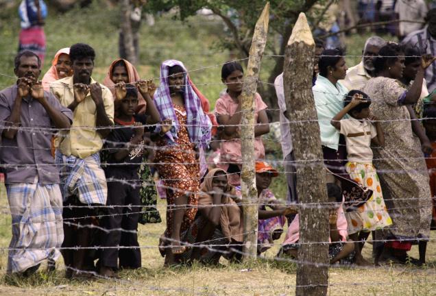 Civilians stand behind the barbed-wire perimeter fence of the Manik Farm refugee camp located on the outskirts of the northern Sri Lankan town of Vavuniya on May 26, 2009.